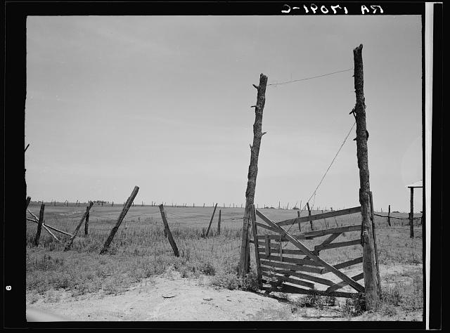 Gate and broken fence before exhausted farmland