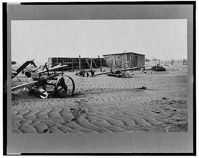 Disused farm implements resting on dust near a shack