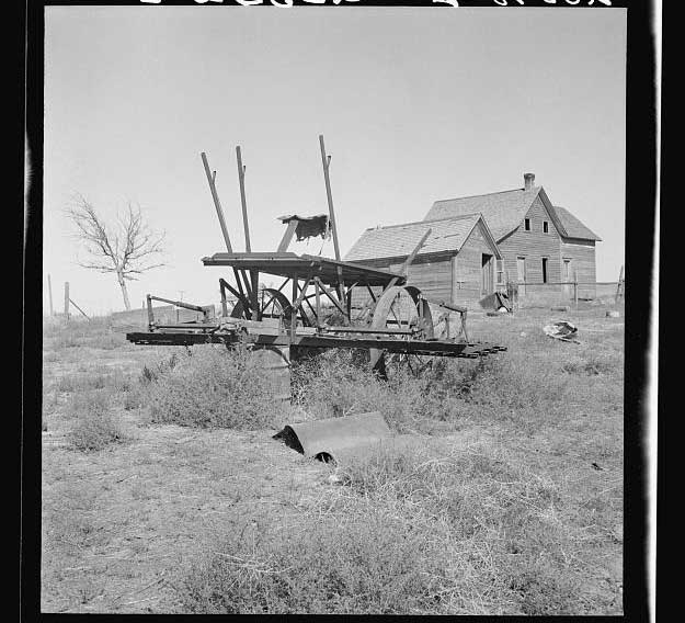 Abandoned farm machinery on scrubby hill; farm house in background